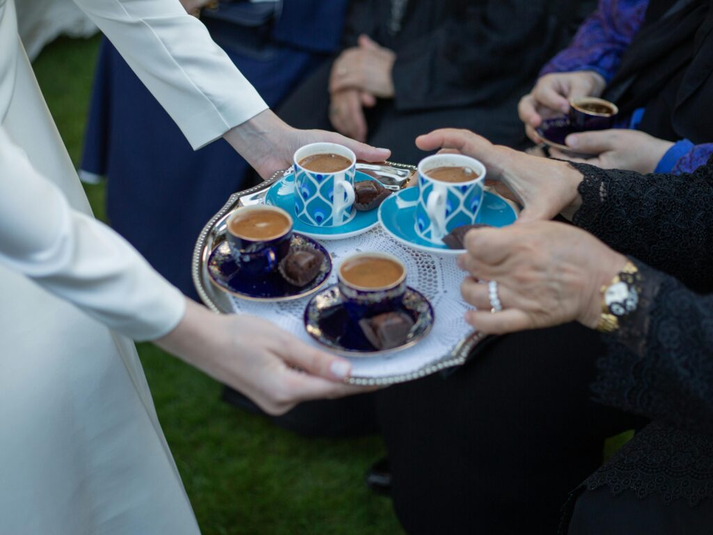 Close-up of a person serving Turkish coffee on a tray with blue cups at a gathering.